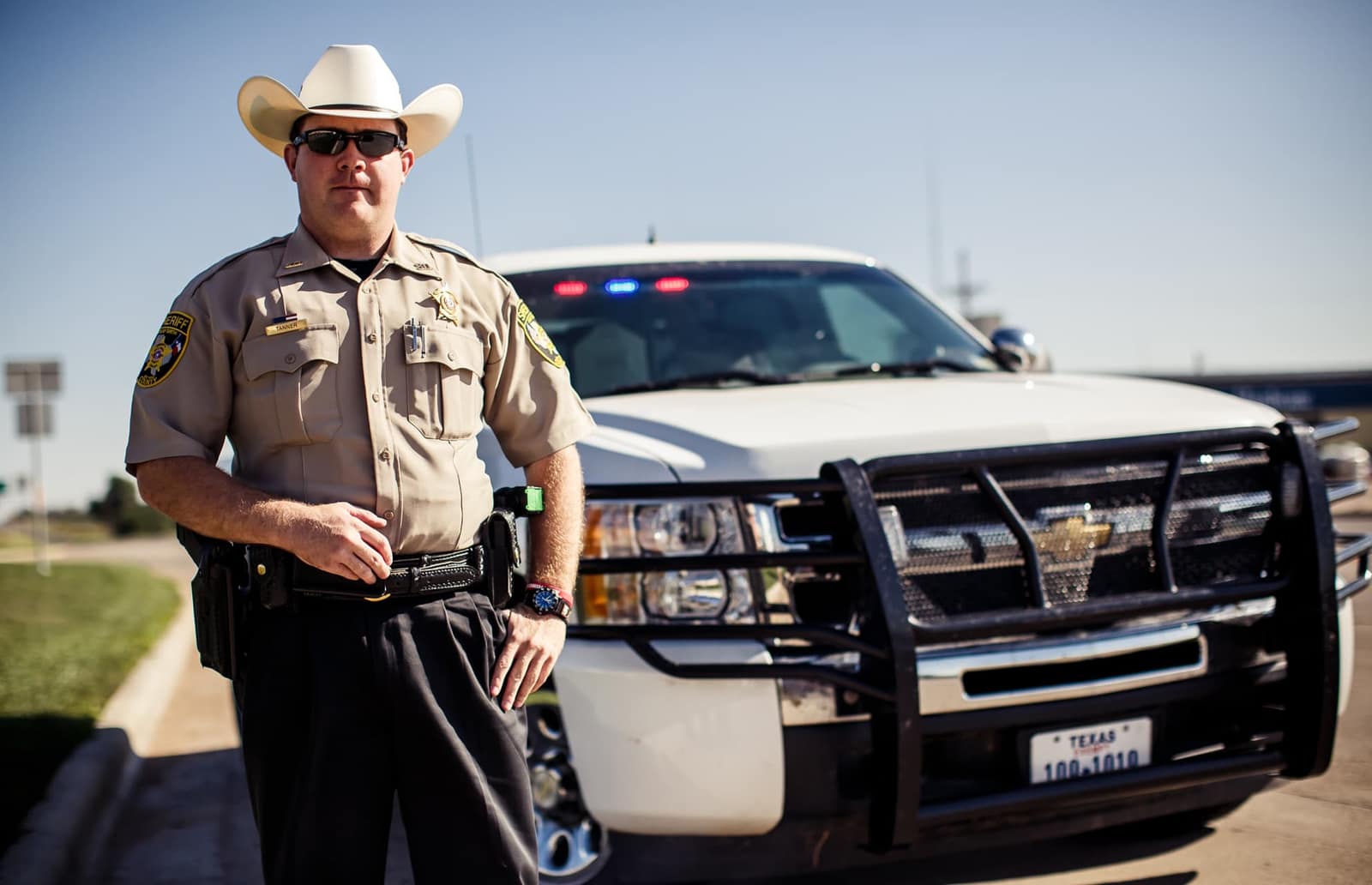 Sheriff’s deputy in a white cowboy hat beside his patrol truck